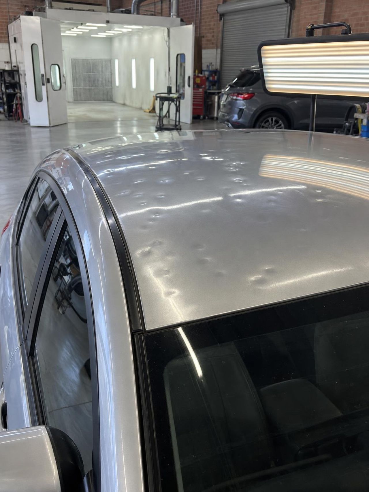 Silver hatchback roof covered in small hail dents under a striped inspection light