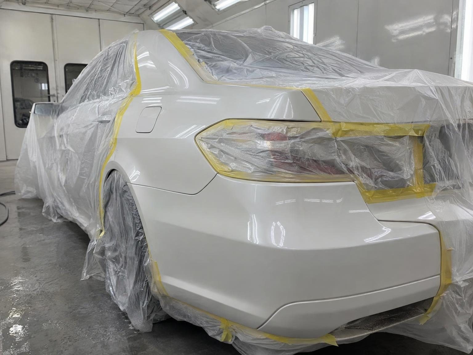 White sedan's rear quarter freshly painted, the rest masked with yellow tape and plastic